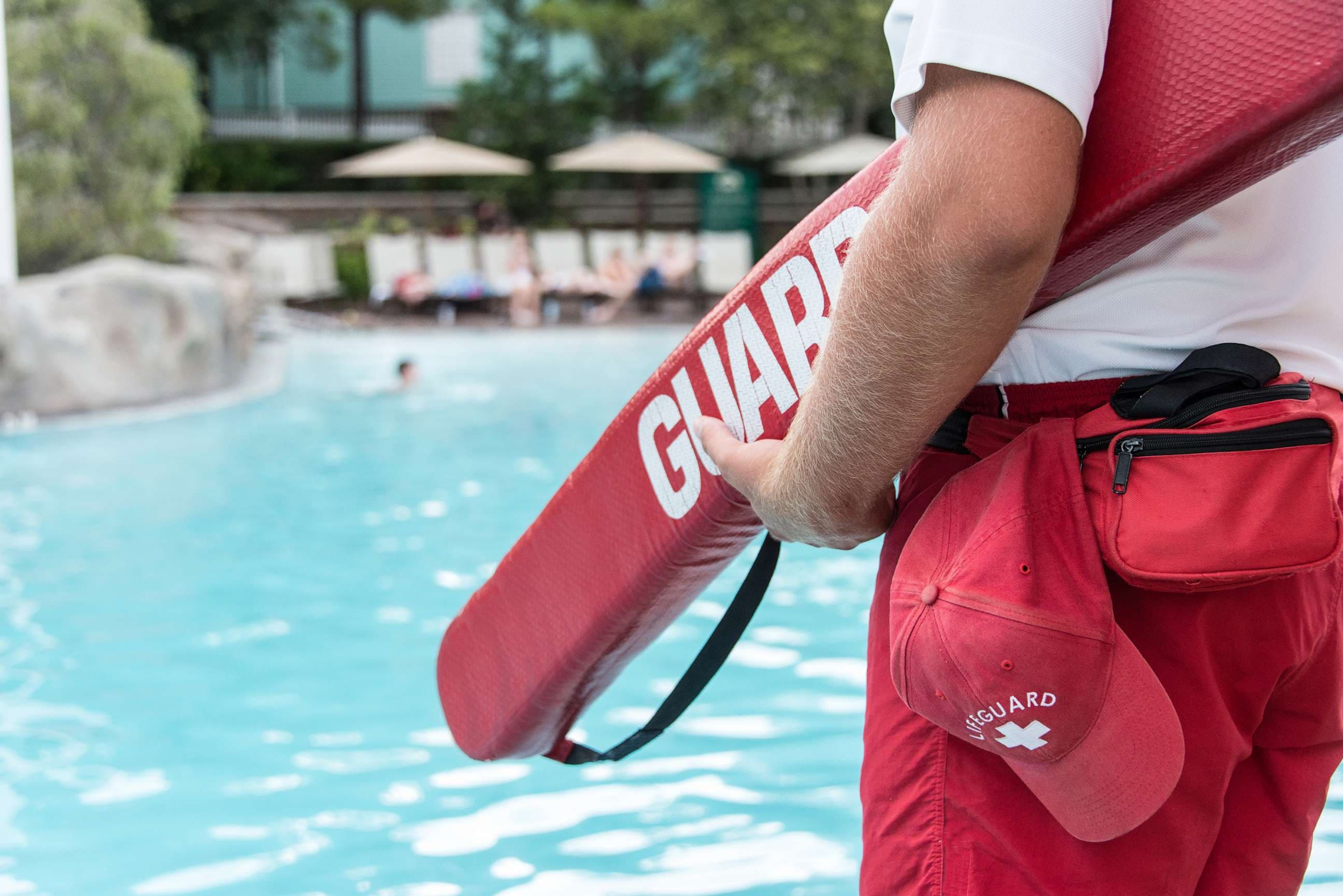 Lifeguard with rescue buoy standing watch at a busy swimming pool facility